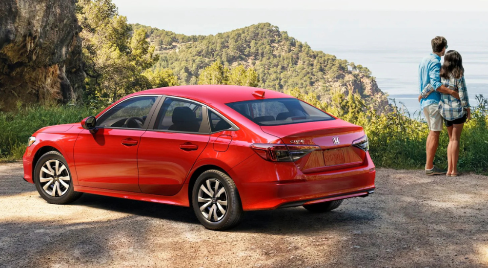 Two people stand next to a red 2026 Honda Civic for sale.