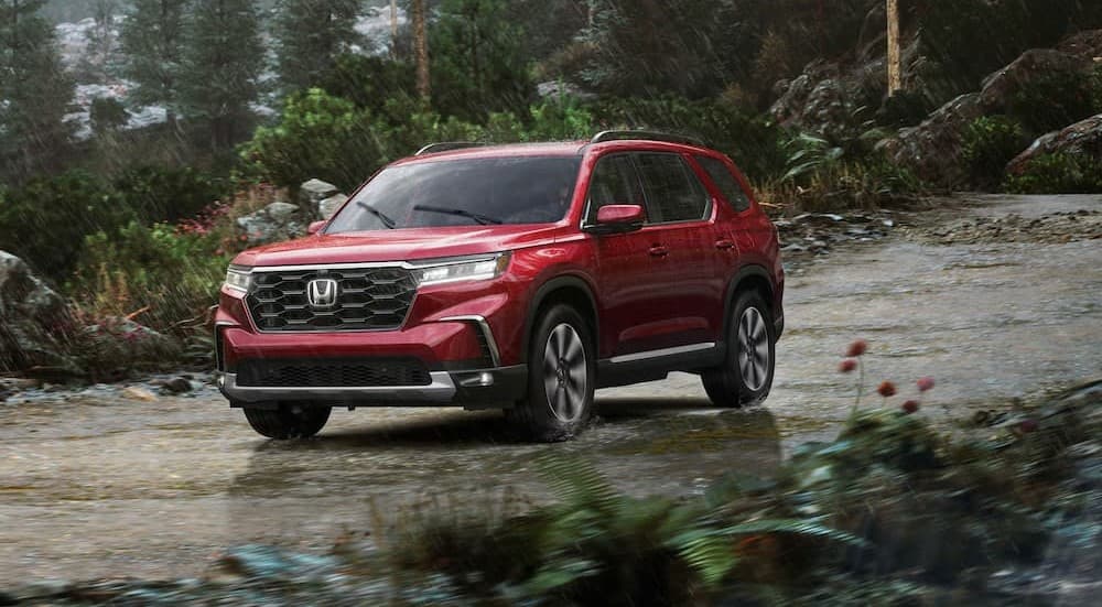 A red 2026 Honda Pilot driving on a rainy day.