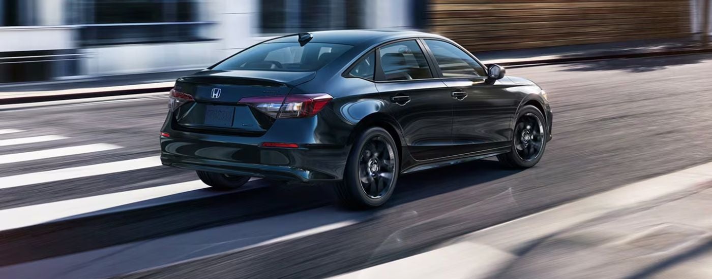 Black 2026 Honda Civic rear view driving on a paved city street.