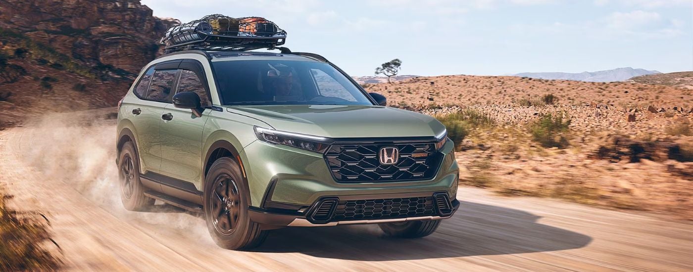 Green 2026 Honda CR-V with camping gear on the roof driving off-road.