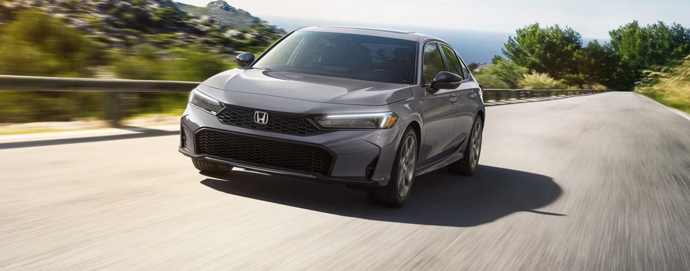 Grey 2026 Honda Civic driving on a paved road.
